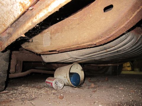 1991 Ford LTD Crown Victoria - The underside of a vehicle, showing a fuel tank and exhaust system, with a discarded beer can and oil filter on the ground.