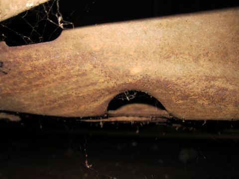 1991 Ford LTD Crown Victoria - A close-up view of a heavily rusted metal component, obscured by cobwebs, with a dark background.