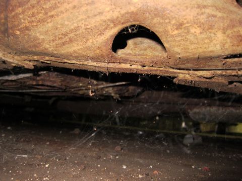 1991 Ford LTD Crown Victoria - The heavily rusted undercarriage of a vehicle is visible, covered in cobwebs and dirt.