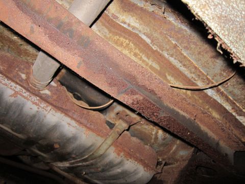 1991 Ford LTD Crown Victoria - The heavily rusted undercarriage of a vehicle displays significant corrosion on its frame and fuel tank.