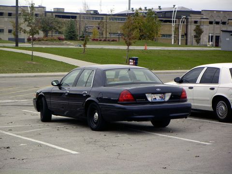 1999 Ford Crown Victoria - Rear view of a dark blue Ford Crown Victoria parked in a lot beside a white car. The Crown Victoria's body style suggests a 2000 model year.