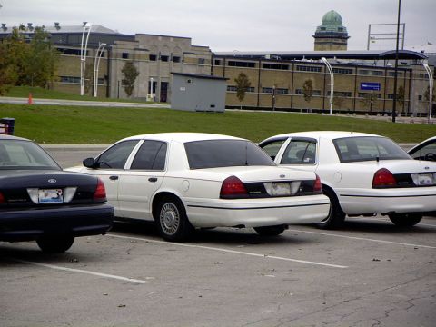 1999 Ford Crown Victoria - Multiple Ford Crown Victorias are parked in a lot with a building in the background.