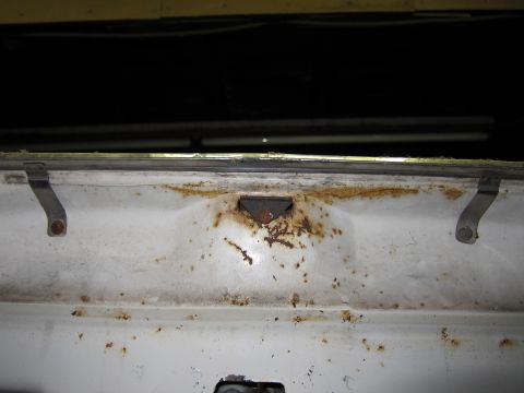 1991 Ford LTD Crown Victoria - Close-up of a rusted white panel with visible metal brackets and a dark interior section.