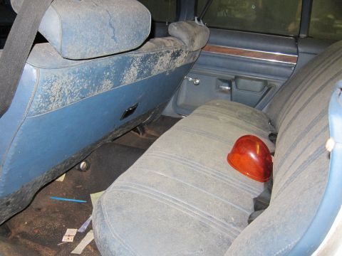 1991 Ford LTD Crown Victoria - The interior of a car shows dusty blue seats and door panels, with a red helmet resting on the rear seat.