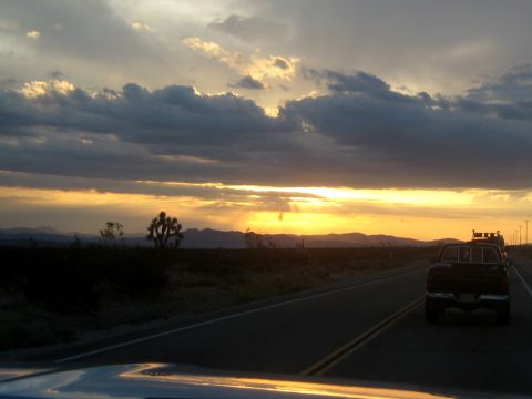 1996 Ford Bronco - A pickup truck travels down a highway as the sun sets over a desert landscape.