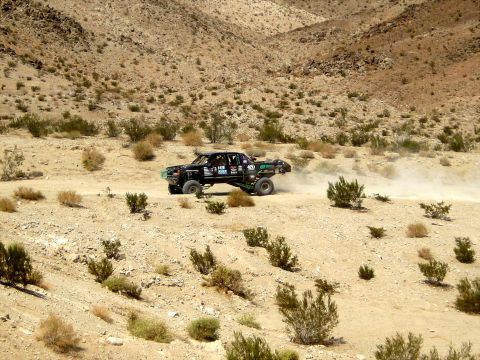 1996 Ford Bronco - A modified truck races through a dusty, arid landscape with sparse vegetation and hills in the background.