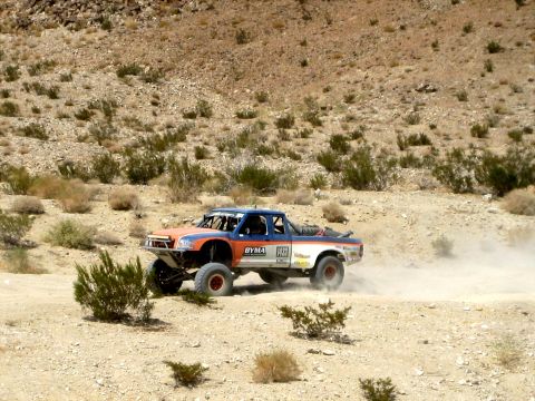 1996 Ford Bronco - A custom off-road truck competes in a desert race, its tires kicking up a cloud of dust.