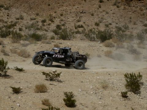 1996 Ford Bronco - A black off-road buggy navigates a dusty desert terrain during a race.