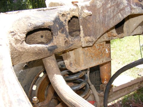 1978 Ford Bronco - Close-up of rusted vehicle frame and suspension components, including a coil spring and shock absorber.