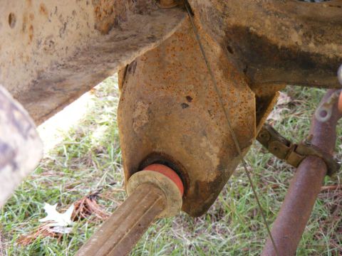 1978 Ford Bronco - Close-up view of heavily rusted suspension components, including a red bushing and a metal clamp, with grass in the background.