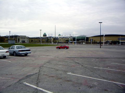 1999 Ford Crown Victoria - A red coupe is parked in a vast, mostly empty parking lot with buildings in the background.