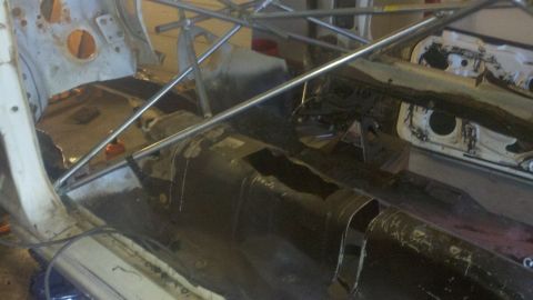 1978 Ford Mustang II - The interior of a vehicle is undergoing extensive modification, with the floor pan exposed and a roll cage fitted.