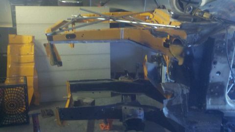 1978 Ford Mustang II - A yellow chassis frame is visible, supported by metal structures and black undercarriage parts, suggesting it is undergoing repair or assem…