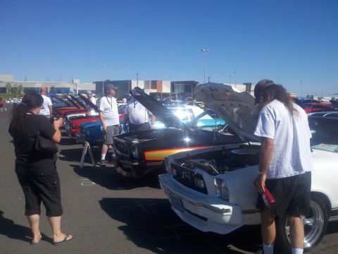 1978 Ford Mustang II - Attendees examine vehicles on display at an outdoor car show under a clear blue sky.