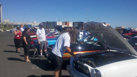 1978 Ford Mustang II - People gather around cars with hoods open at an outdoor car show on a sunny day.
