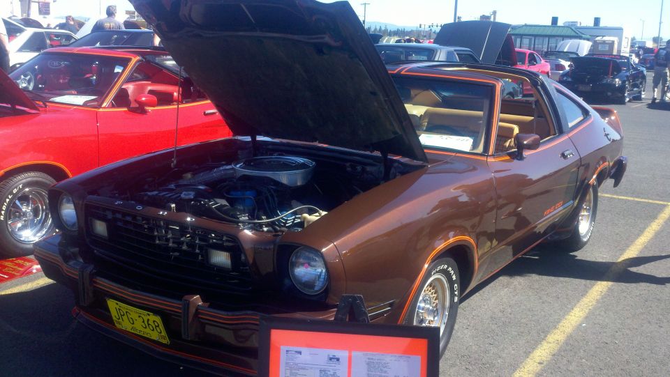 Brown 1978 Ford Mustang II with hood open, parked next to a red car