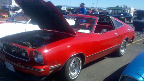 1978 Ford Mustang II - A red coupe with its hood open at an outdoor car show, displaying its engine and interior.