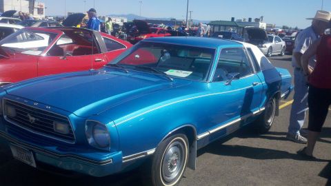 1978 Ford Mustang II - A blue 1978 Ford Mustang II coupe with a white roof is parked at a car show, with other vehicles visible in the background.