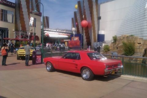 1991 Ford LTD Crown Victoria - A red 1967 Ford Mustang coupe is parked in front of a building with a yellow car visible behind it.