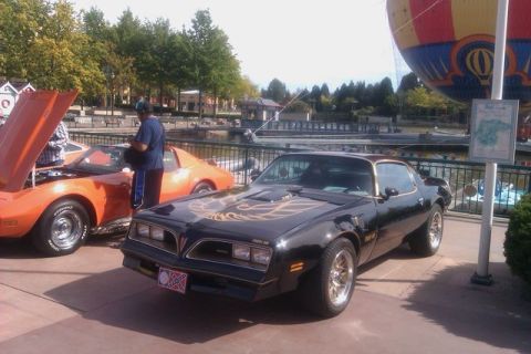 1991 Ford LTD Crown Victoria - A black 1977 Pontiac Firebird Trans Am is parked next to an orange car, with a hot air balloon in the background.