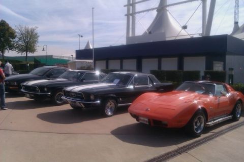 1991 Ford LTD Crown Victoria - A row of classic American muscle cars, including a C3 Corvette and multiple Mustangs, are parked outside a building.