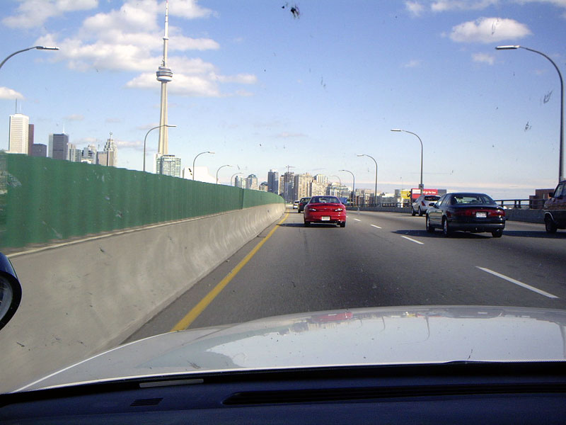 Red sedan driving on a highway with Toronto skyline in background