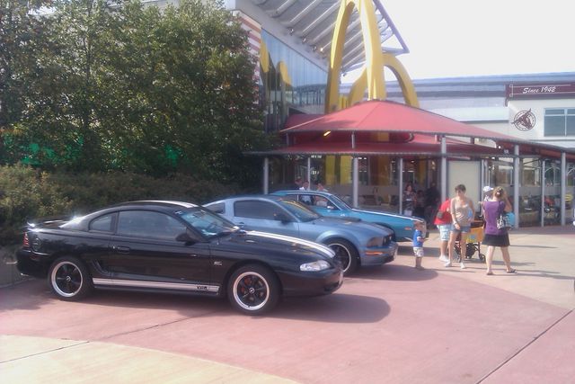 Black Ford Mustang parked in front of a McDonald's with two other Mustangs behind it