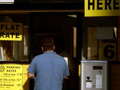 1999 Ford Crown Victoria - A person stands before a parking pay station, with signs indicating rates and flat fees.