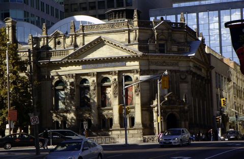 1999 Ford Crown Victoria - Cars drive past a grand building with architectural details and banners.