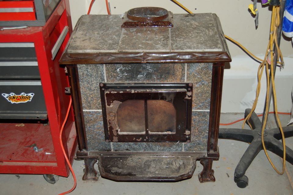 Wood stove with tiled facade and glass door, next to a red tool chest