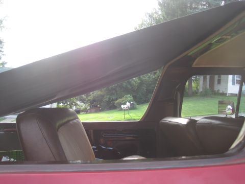 1979 Ford Bronco - Interior view of a red vehicle with brown seats and a soft top, showing the rear seating area and a glimpse of the outdoors.