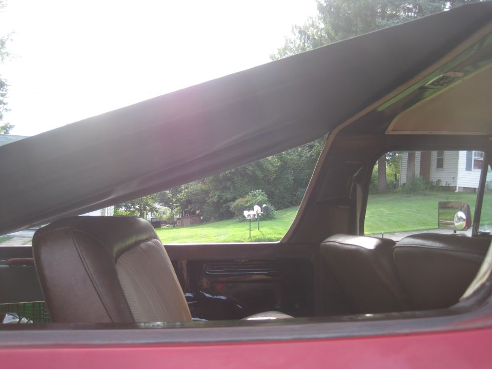 Red vehicle interior with brown seats and a dark soft top, viewed from the side