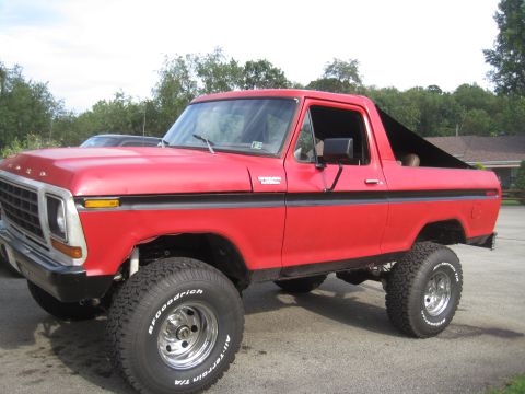 1979 Ford Bronco - This red 1979 Ford Bronco features a lifted suspension and off-road tires, with a black soft top covering the rear.