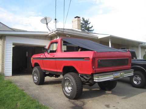 1979 Ford Bronco - Red lifted late-1970s Ford Bronco with black soft top and chrome wheels parked in a residential driveway.