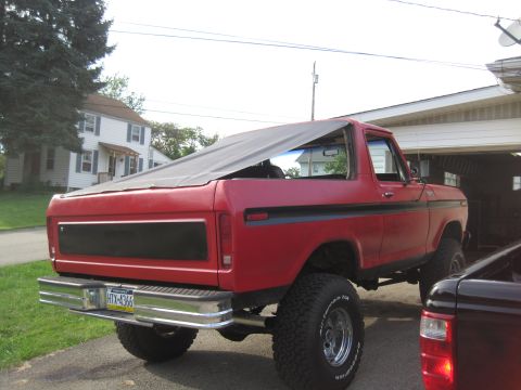 1979 Ford Bronco - The rear view of a red 1979 Ford Bronco shows its lifted suspension and a soft top covering the rear.