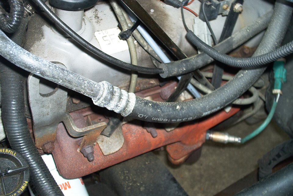 Engine bay with rusty exhaust manifold, oxygen sensor, and worn hoses