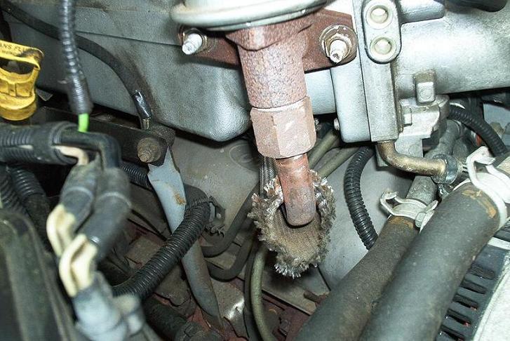 Rusty threaded steel tube with frayed braided shield among hoses and wiring in an engine bay