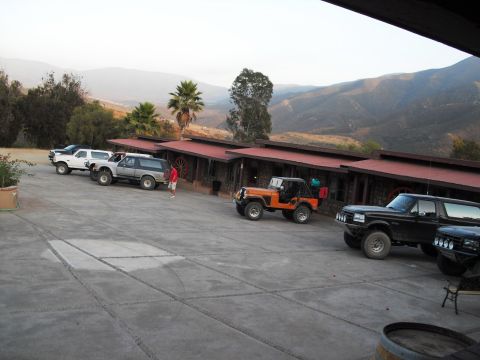 1986 Ford Bronco - Several off-road vehicles are parked in front of a building with a mountainous landscape behind them.