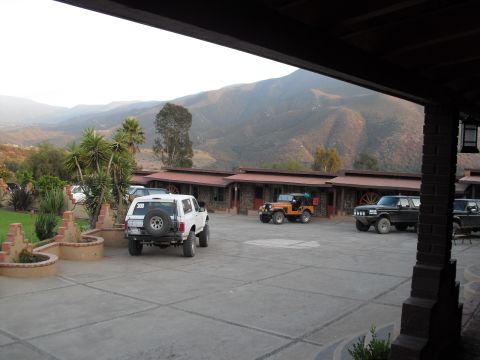 1986 Ford Bronco - Multiple SUVs and a pickup truck are parked in a lot outside motel rooms with mountains in the background.