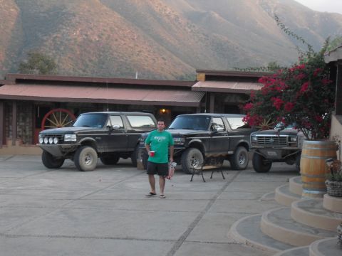 1986 Ford Bronco - Three Ford Bronco SUVs are parked in a courtyard with a man standing in front of the middle vehicle.