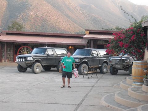 1986 Ford Bronco - Three modified Ford Broncos are parked in a courtyard with a man standing between two of them.