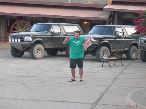 1986 Ford Bronco - A man stands between two dark SUVs, one of which features a custom front bumper and auxiliary lights.