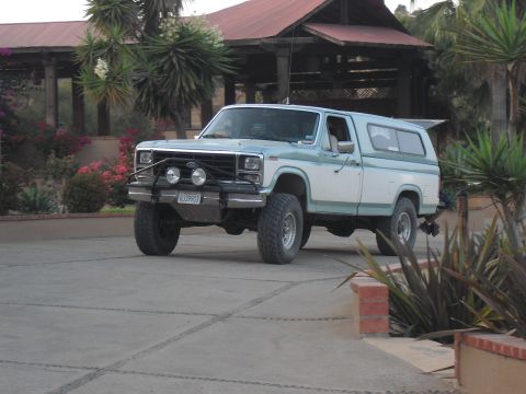 1986 Ford Bronco - This two-tone pickup truck features a camper shell and aftermarket off-road modifications.