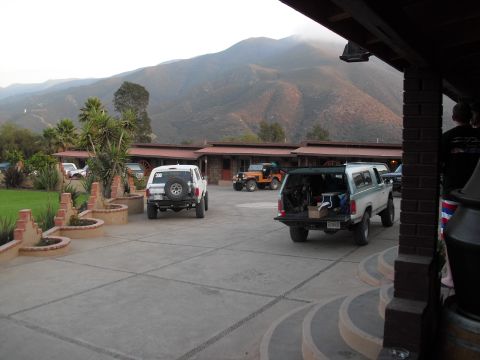 1986 Ford Bronco - A two-tone Ford Bronco with its tailgate down is parked in front of a motel, with mountains in the background.