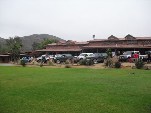 1986 Ford Bronco - Multiple Ford Broncos and other SUVs are parked in front of a building on a cloudy day.