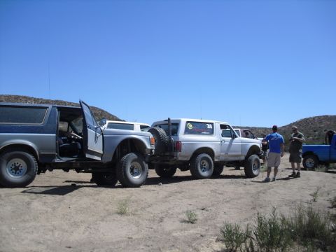 1986 Ford Bronco - Several off-road vehicles are parked on a dusty terrain with people standing around them.