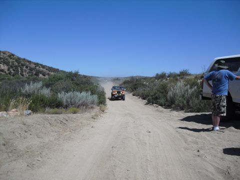 1986 Ford Bronco - Off-road vehicles navigate a dusty trail in a remote, arid environment.
