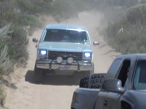 1986 Ford Bronco - A 1986 Ford Bronco navigates a dusty trail, followed closely by another vehicle.