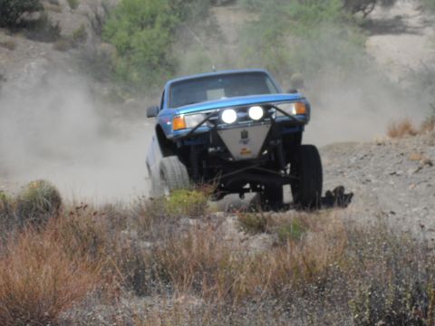 1986 Ford Bronco - Off-road truck navigates a dusty trail in a dry, arid landscape.