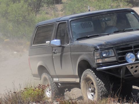 1986 Ford Bronco - This modified Ford Bronco is navigating a dusty trail with off-road lights and a custom bumper.